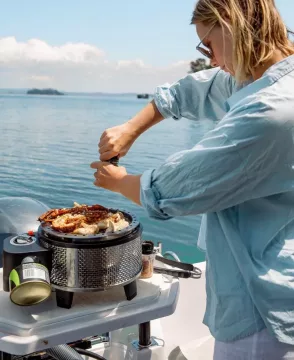 Kvinne som kverner pepper over mat som stekes på en Cobb grillpanne.